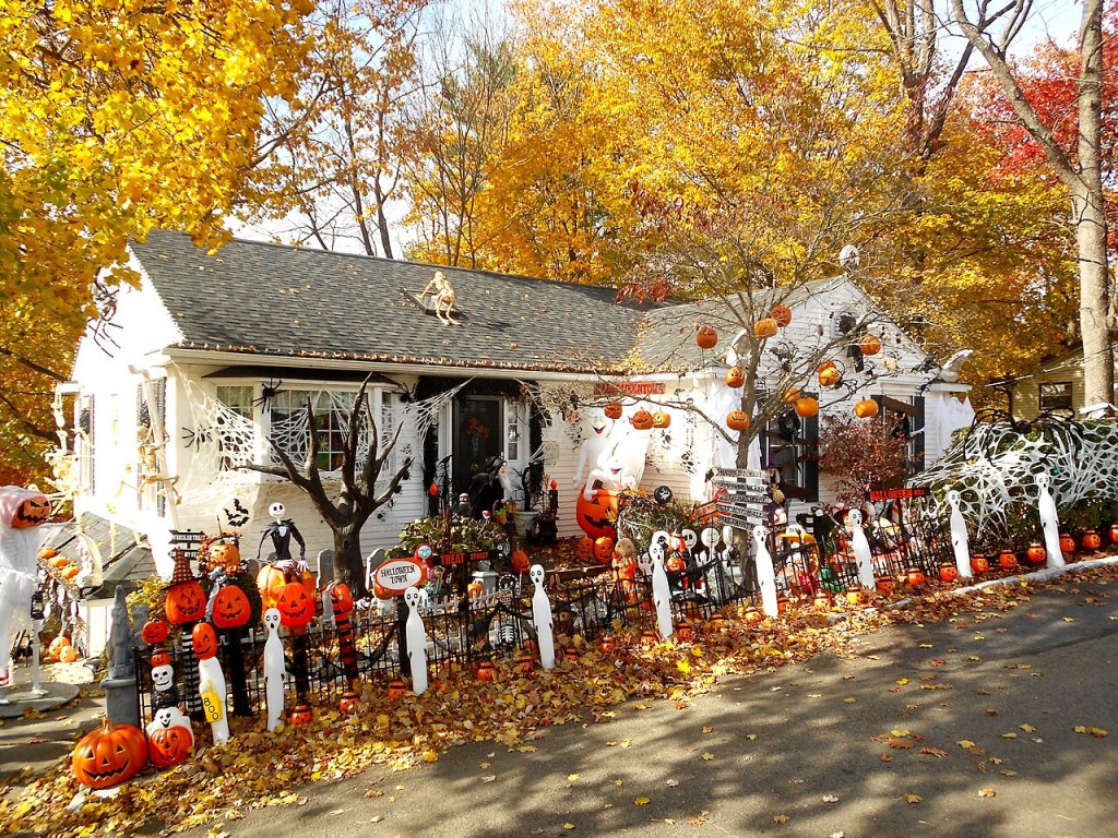 Casa decorada para Halloween con calabazas, fantasmas y telarañas, rodeada de árboles con hojas de otoño.